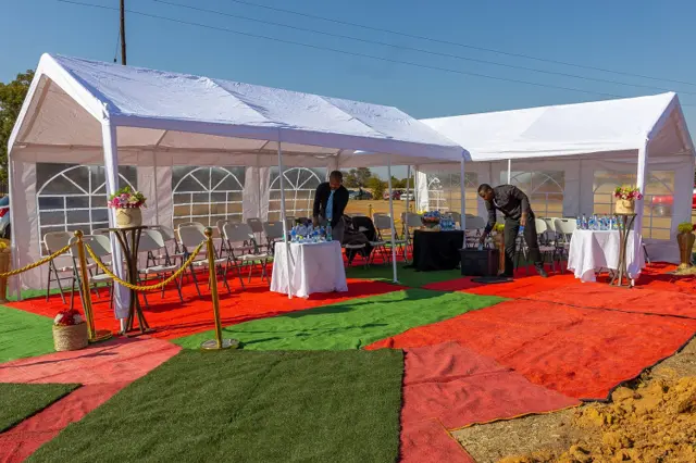 A Mashigo graveside setup with a white tent, seating and floral arrangements on red and green carpeting
